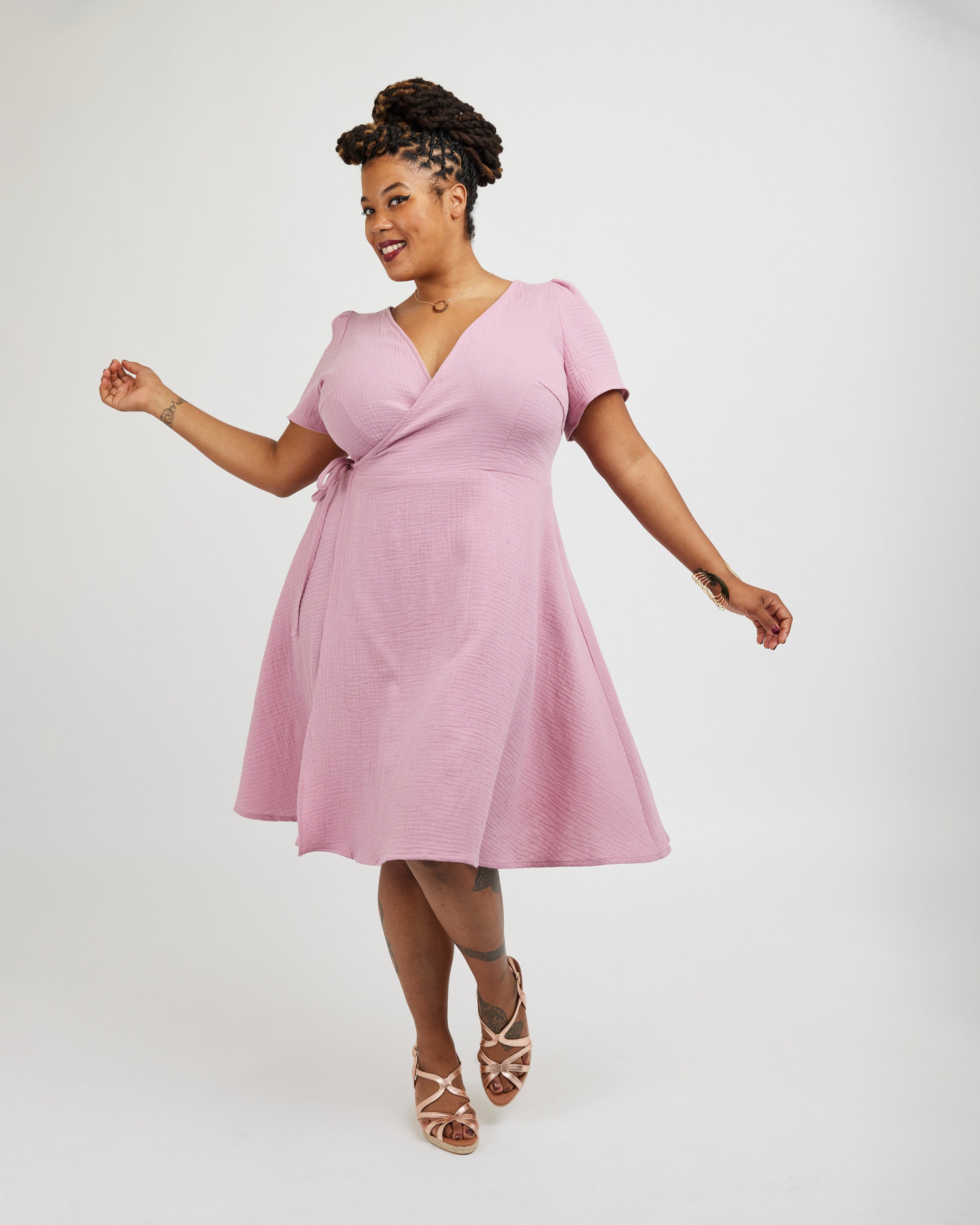 Woman wearing a pink dress on a white background. This dress is the Roseclair Wrap Dress sewing pattern from Cashmerette.
