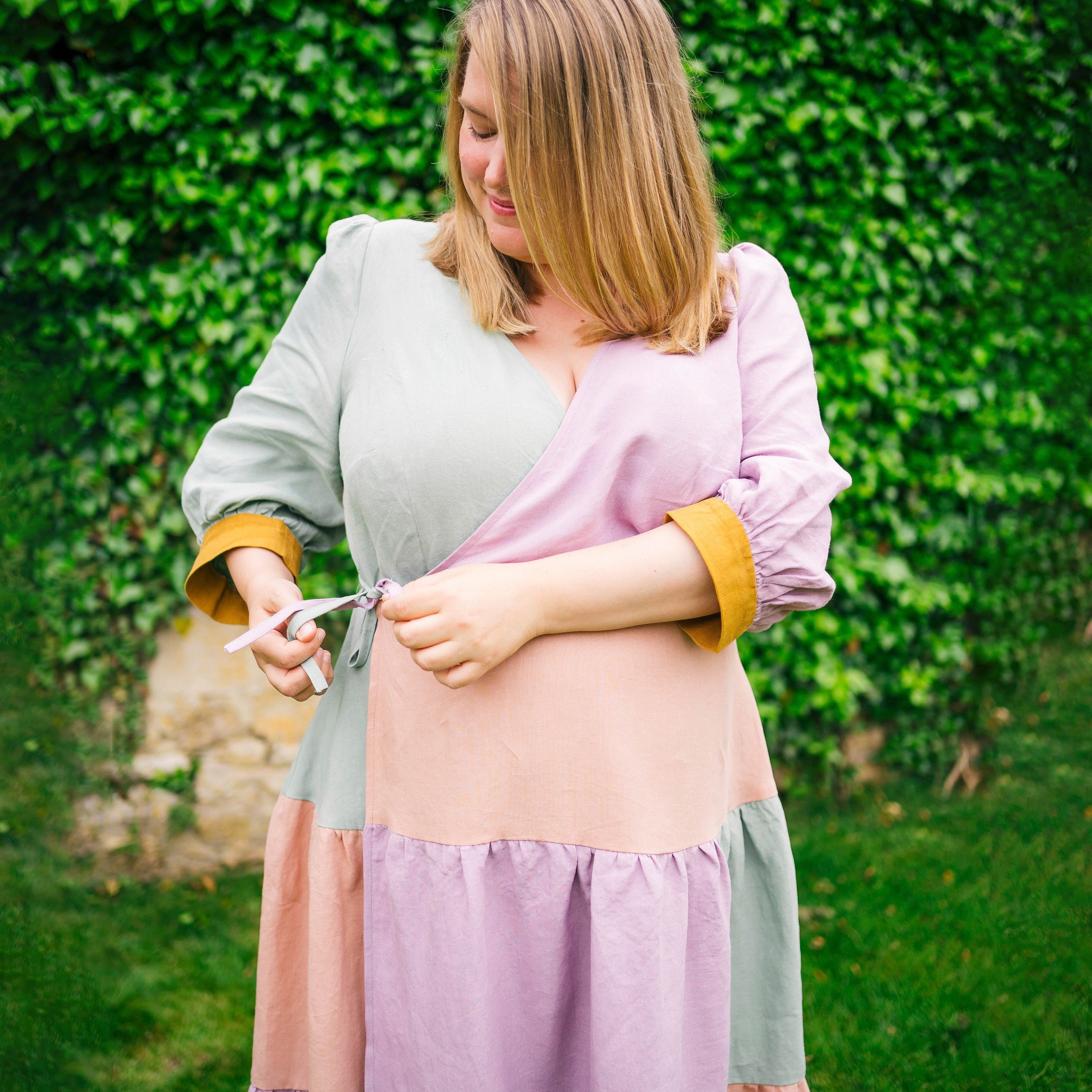 Woman in a layered outfit with a green background. This dress is the Roseclair Wrap Dress sewing pattern from Cashmerette.