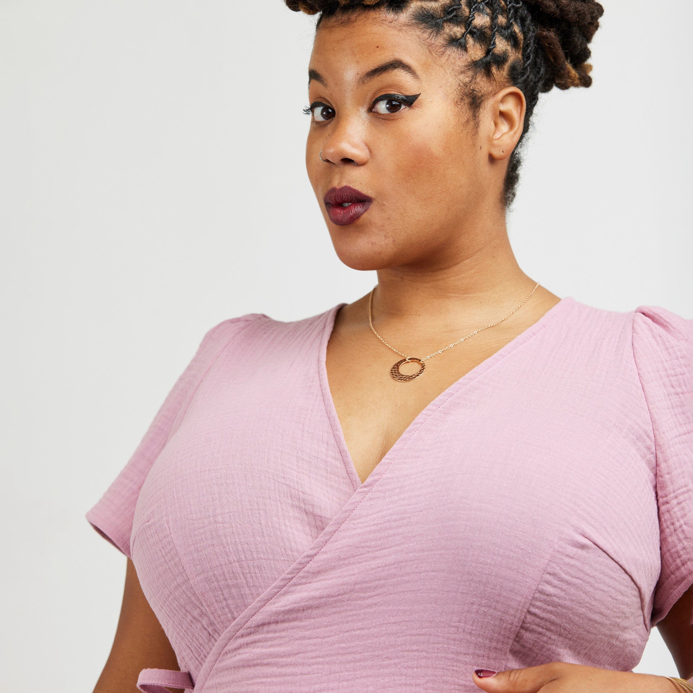 Woman wearing a pink dress against a white background. This dress is the Roseclair Wrap Dress sewing pattern from Cashmerette.
