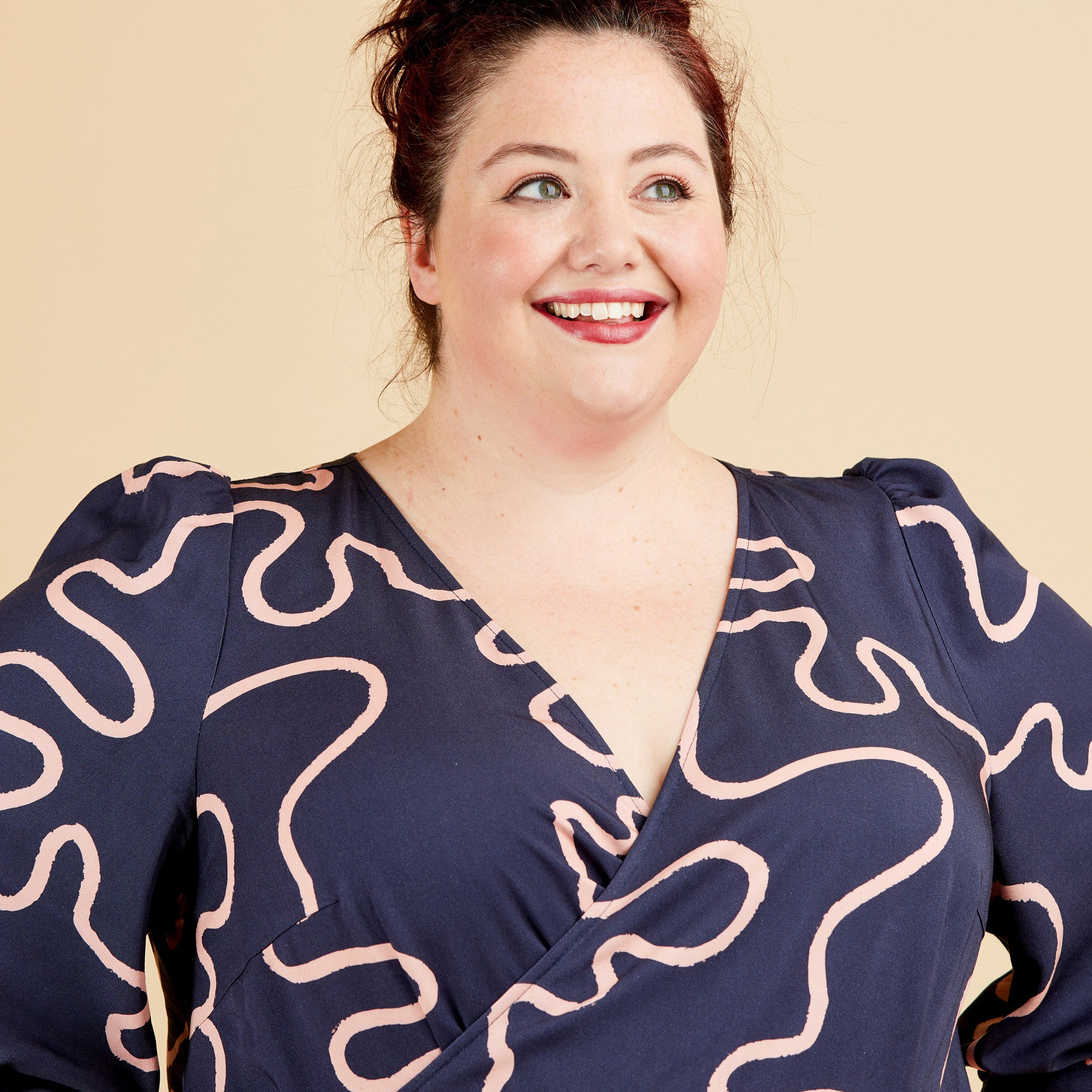 Woman wearing a navy dress with white pattern against a beige background. This dress is the Roseclair Wrap Dress sewing pattern from Cashmerette.