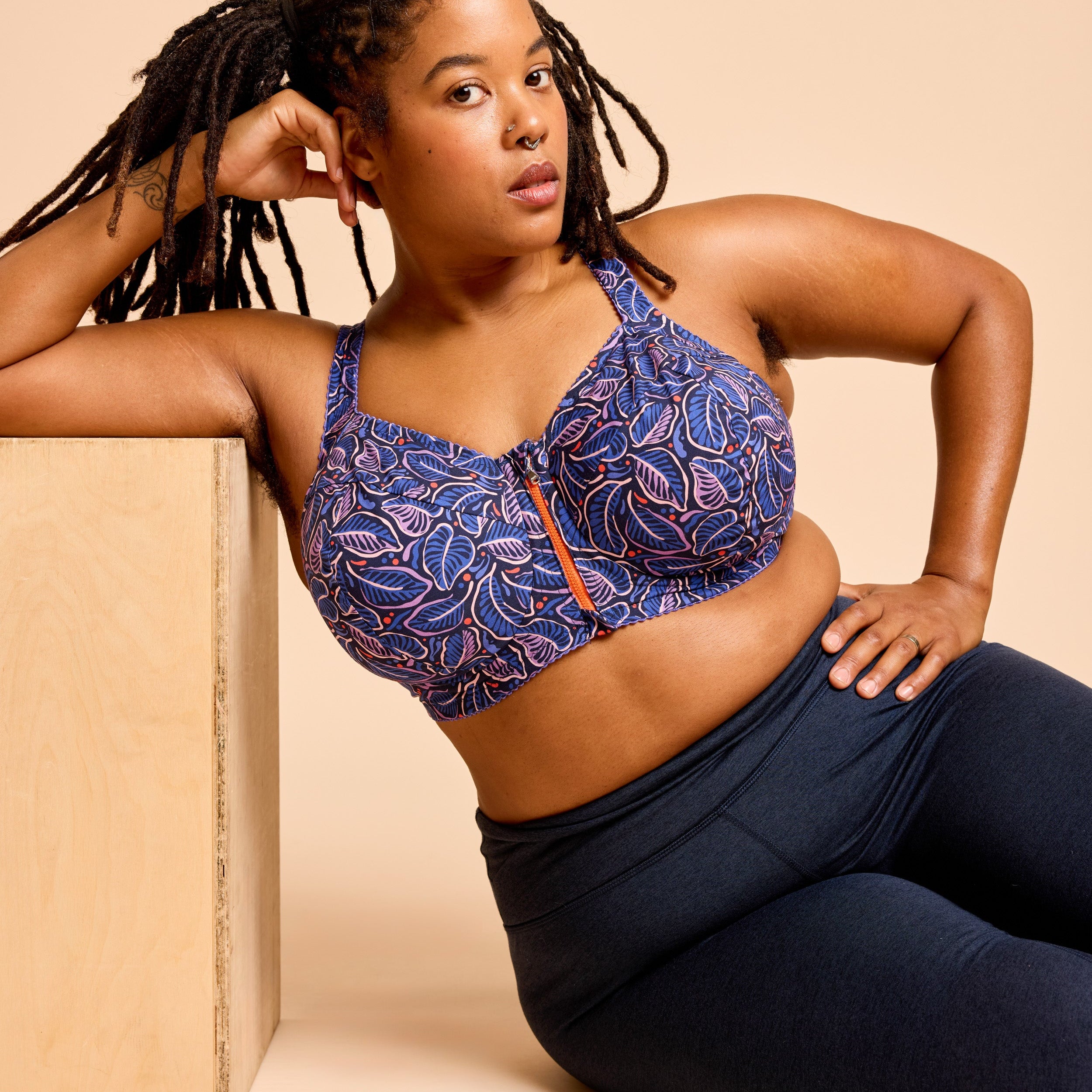 Woman wearing a blue patterned sports bra and navy leggings against a beige background. This is the Cashmerette Somerville Sports Bra sewing pattern for big boobs.