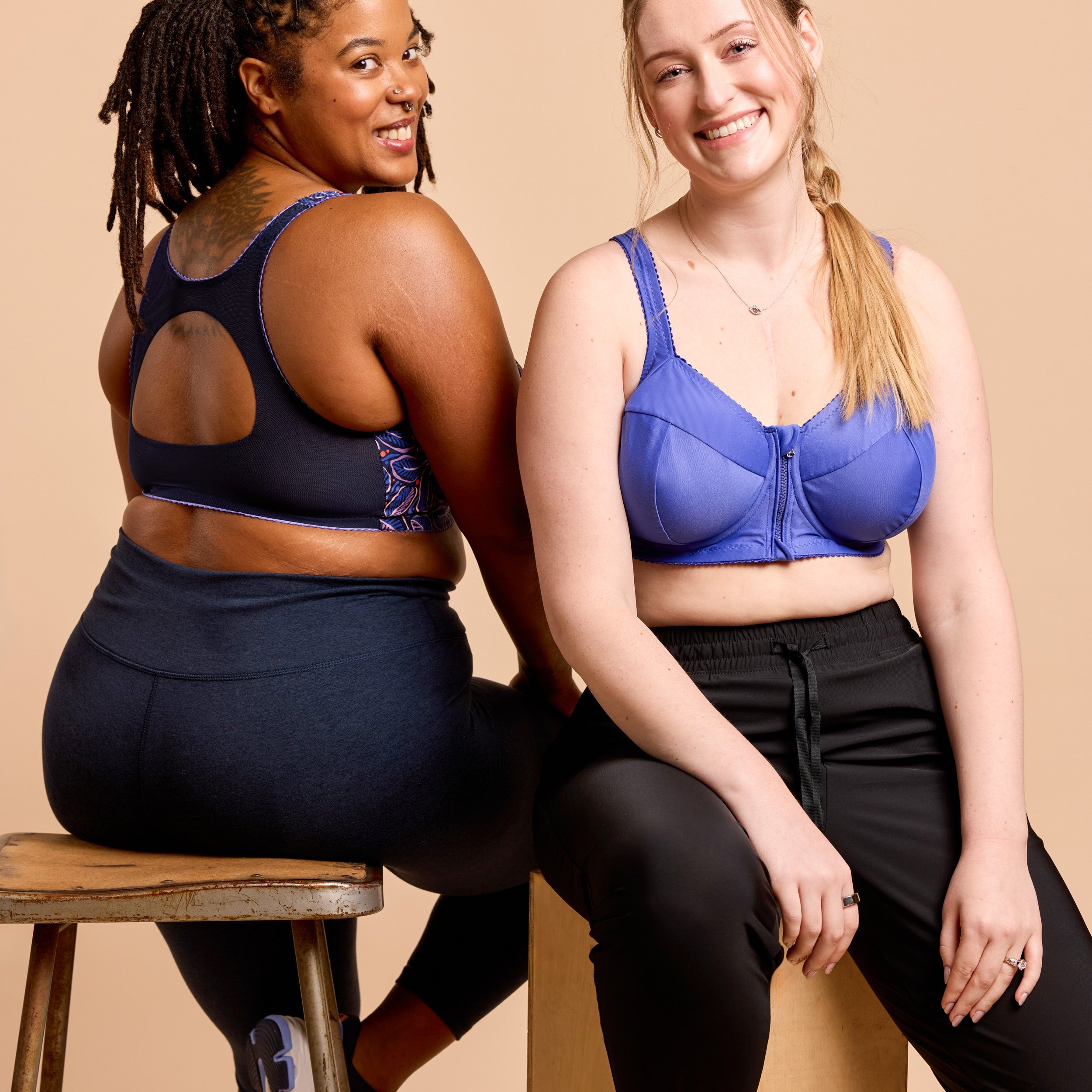 Two women sitting on a stool wearing sports bras and leggings against a beige background. This is the Cashmerette Somerville Sports Bra sewing pattern for big boobs.