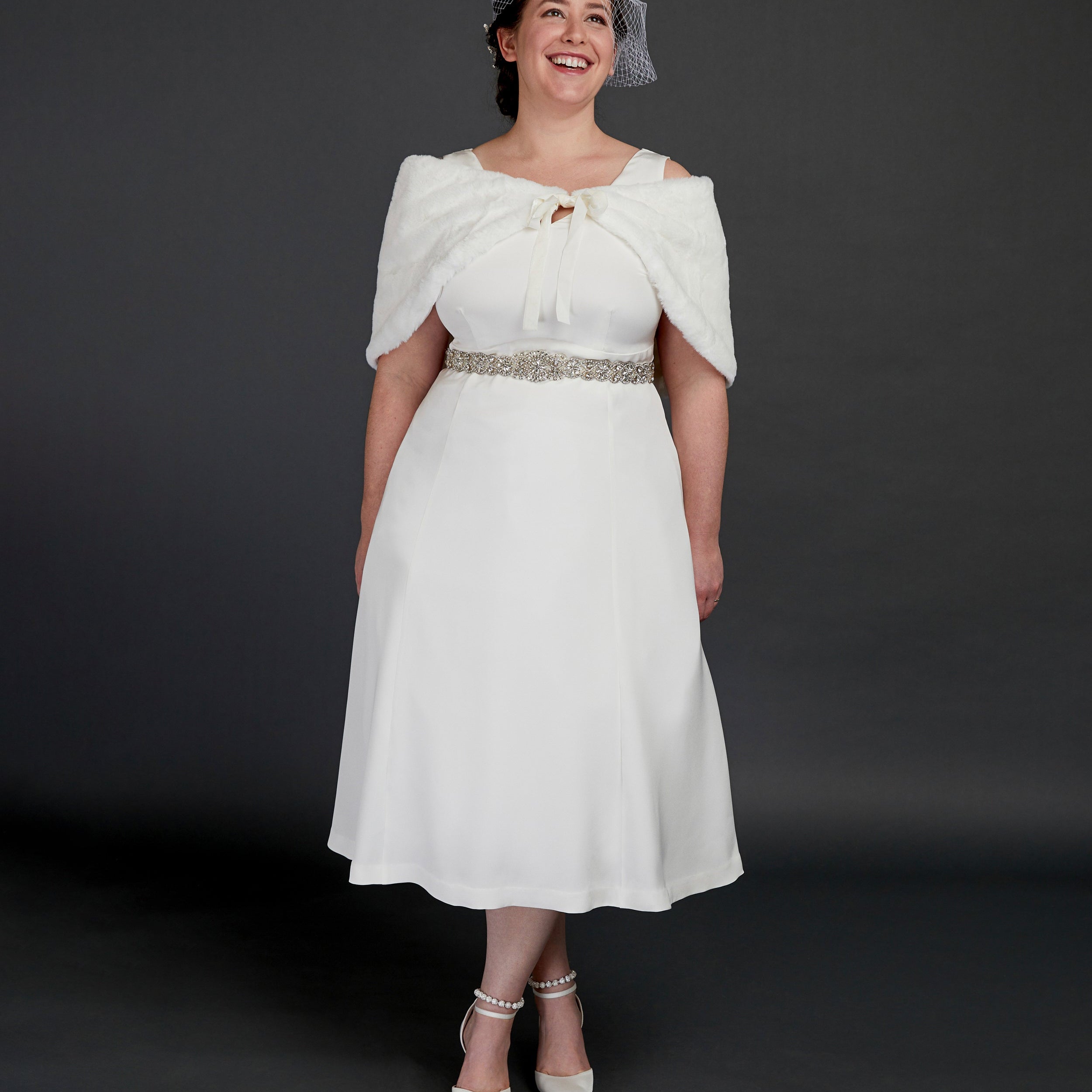 Woman wearing a white dress with a fur shrug and hat against a dark background. This dress is the Upton Dress & Skirt sewing pattern from Cashmerette.