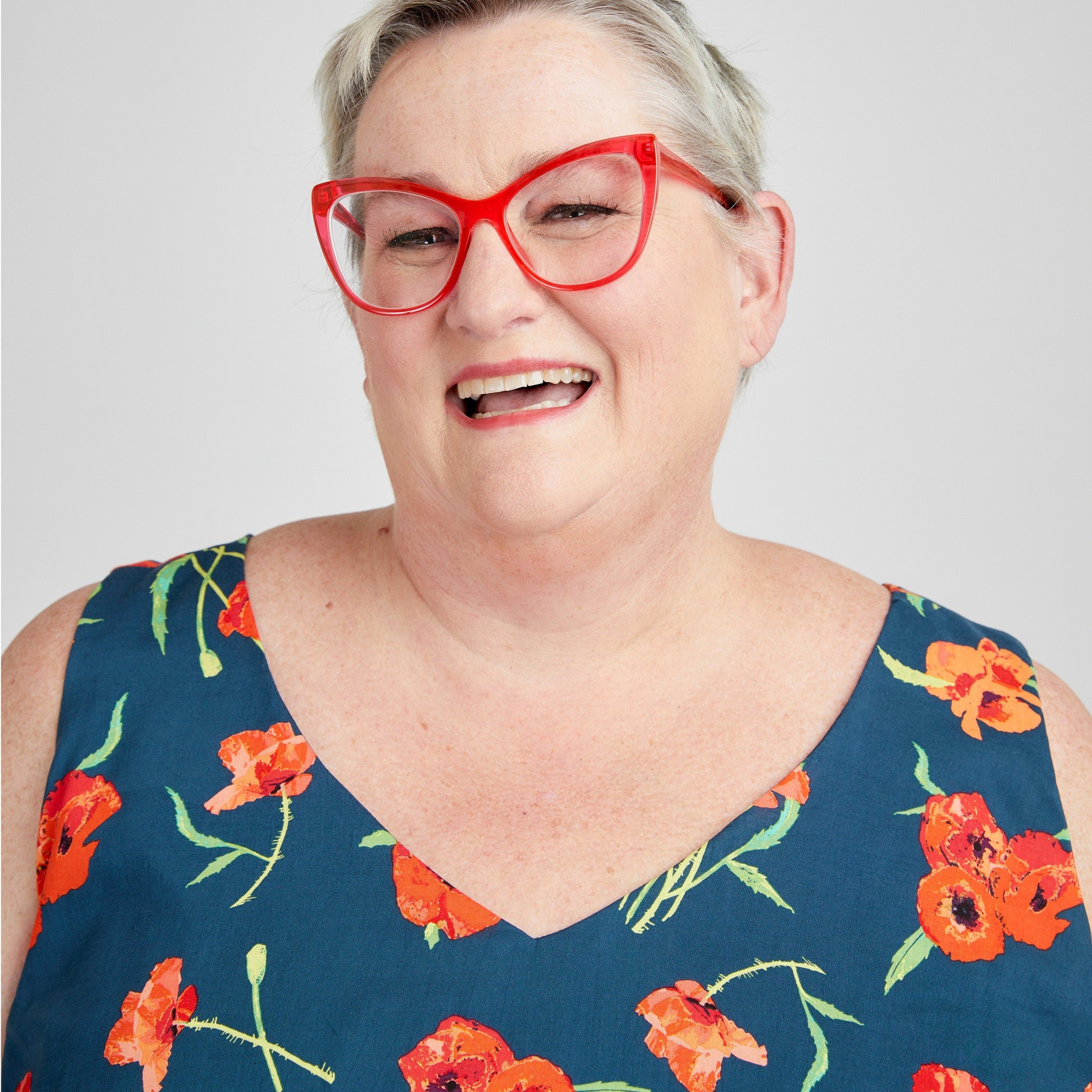 Person wearing a blue floral dress with red glasses on a white background. This dress is the Upton Dress & Skirt sewing pattern from Cashmerette.