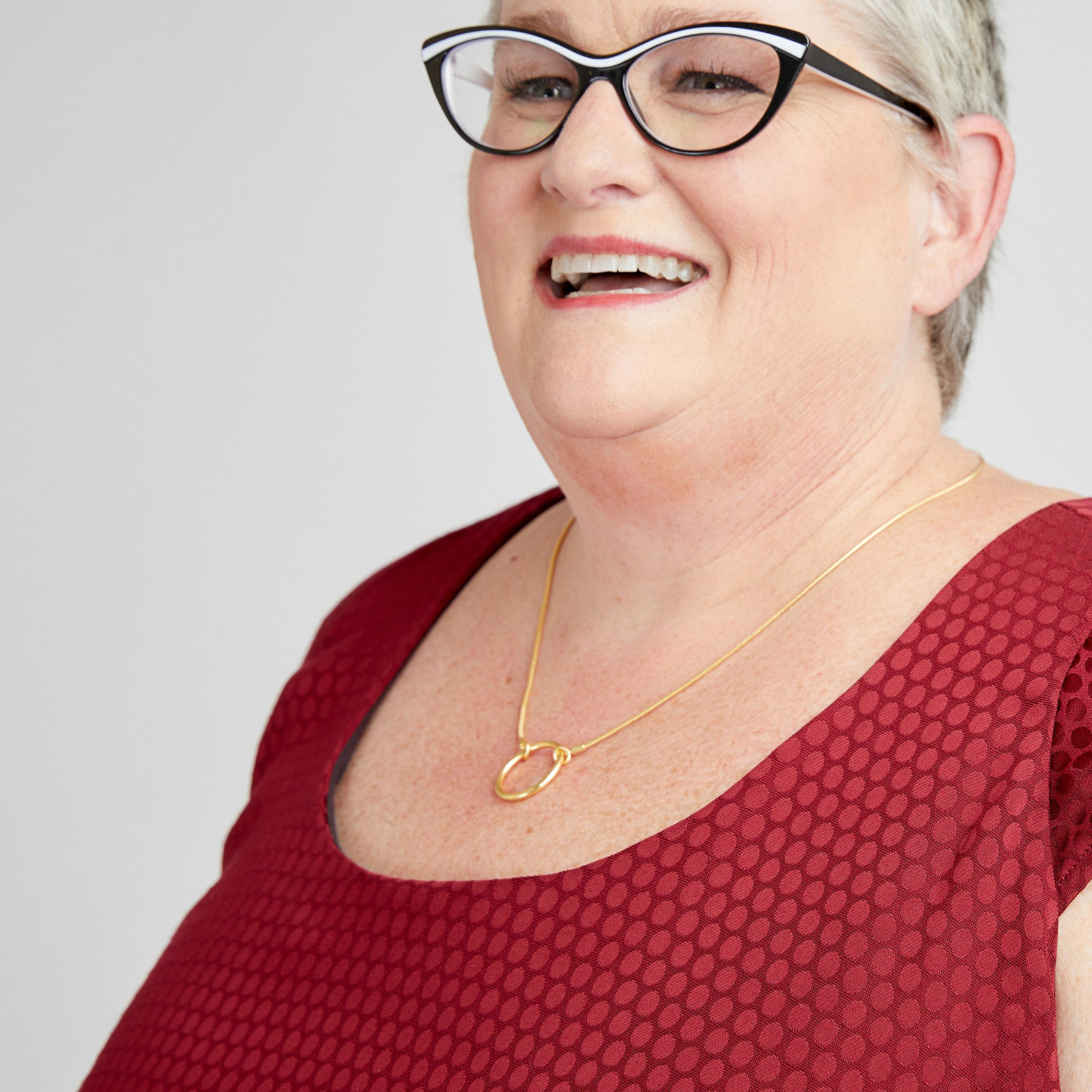 Woman wearing glasses and a red top with a gold necklace on a white background. This dress is the Upton Dress & Skirt sewing pattern from Cashmerette.