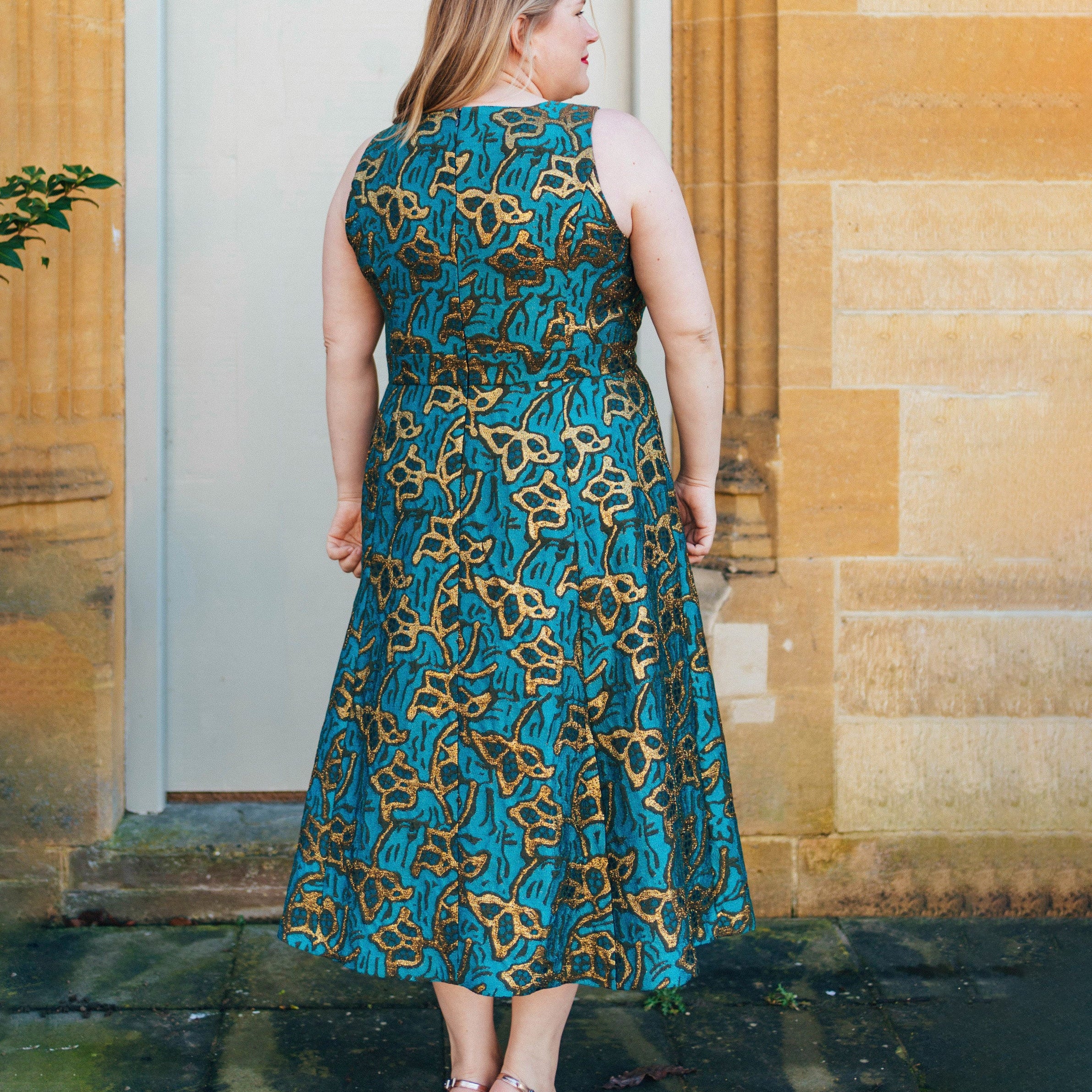 Woman wearing a blue and gold patterned dress standing in front of a stone building.. This dress is the Upton Dress & Skirt sewing pattern from Cashmerette.