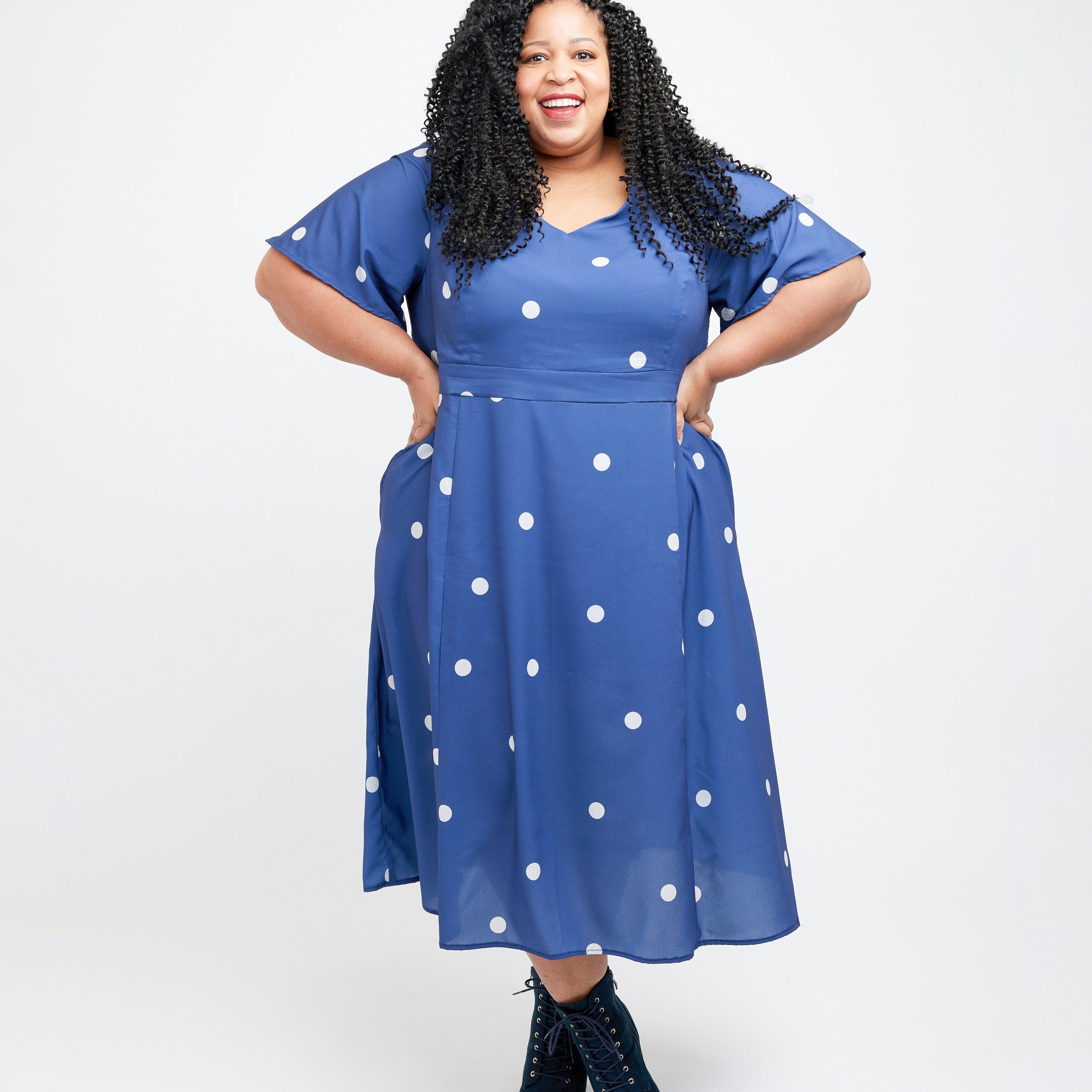 Woman wearing a blue dress with white polka dots on a white background. This dress is the Upton Dress & Skirt sewing pattern from Cashmerette.