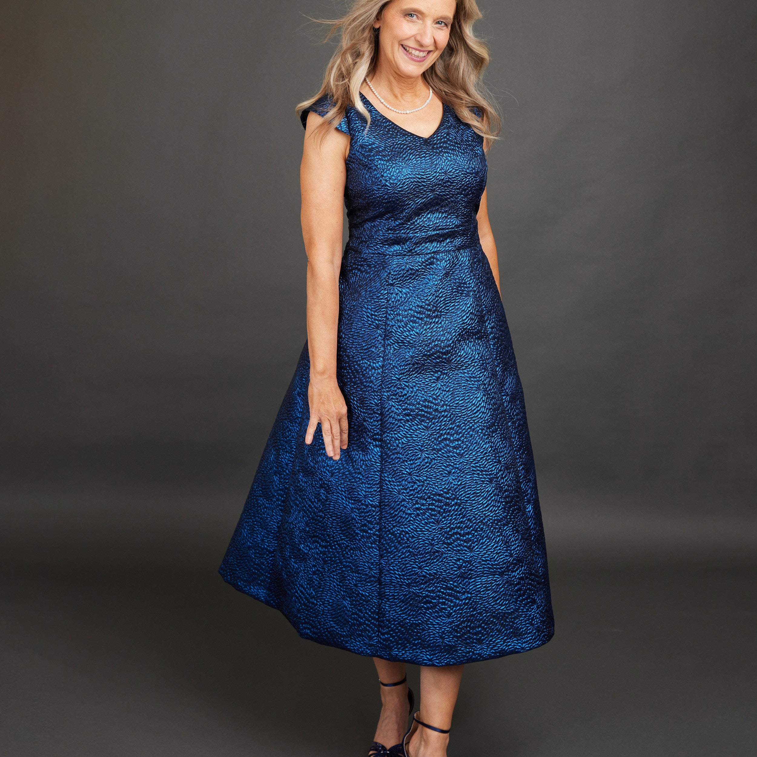 Woman wearing a blue dress against a gray background. This dress is the Upton Dress & Skirt sewing pattern from Cashmerette.