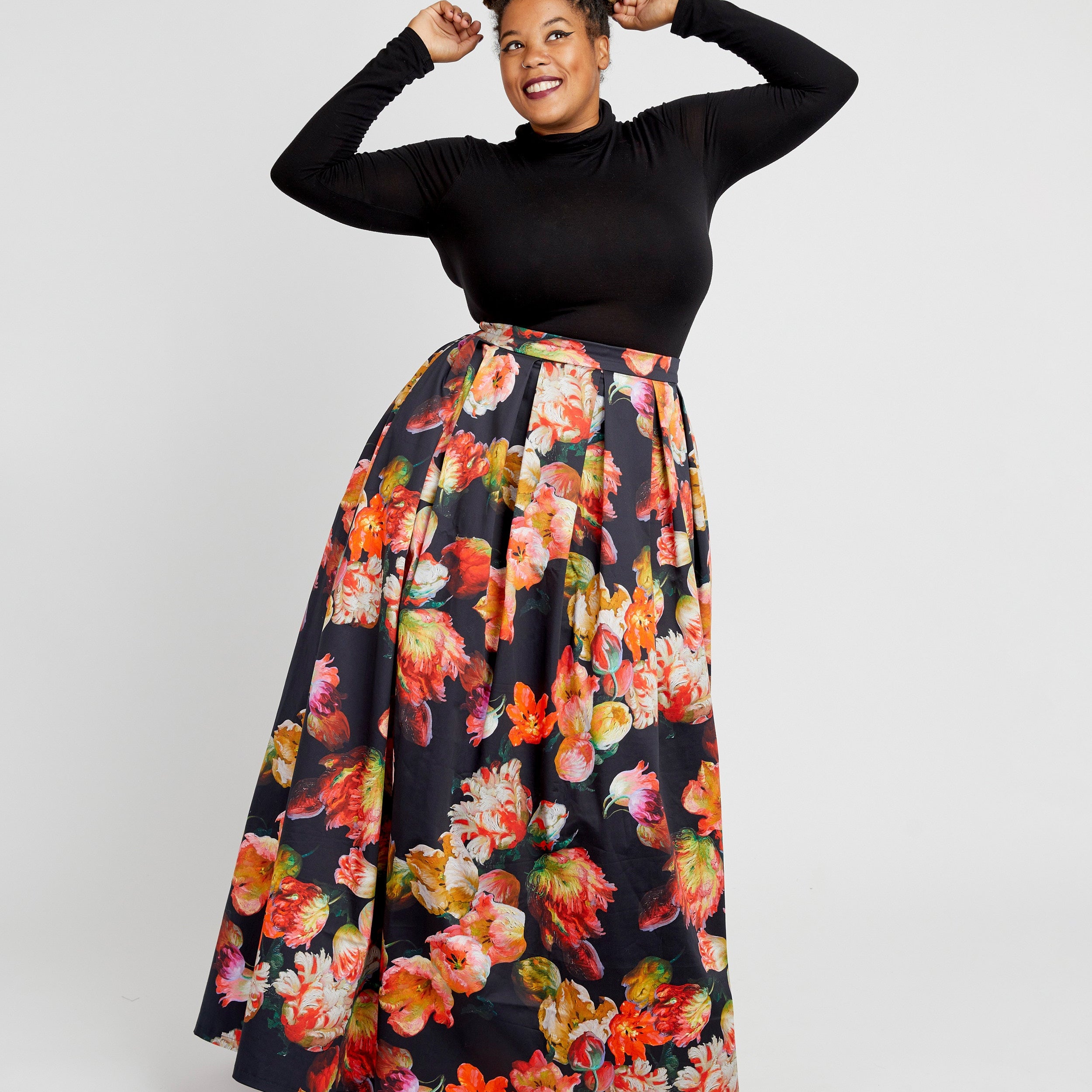 Woman wearing a black long-sleeve top and floral skirt on a white background. This dress is the Upton Dress & Skirt sewing pattern from Cashmerette.