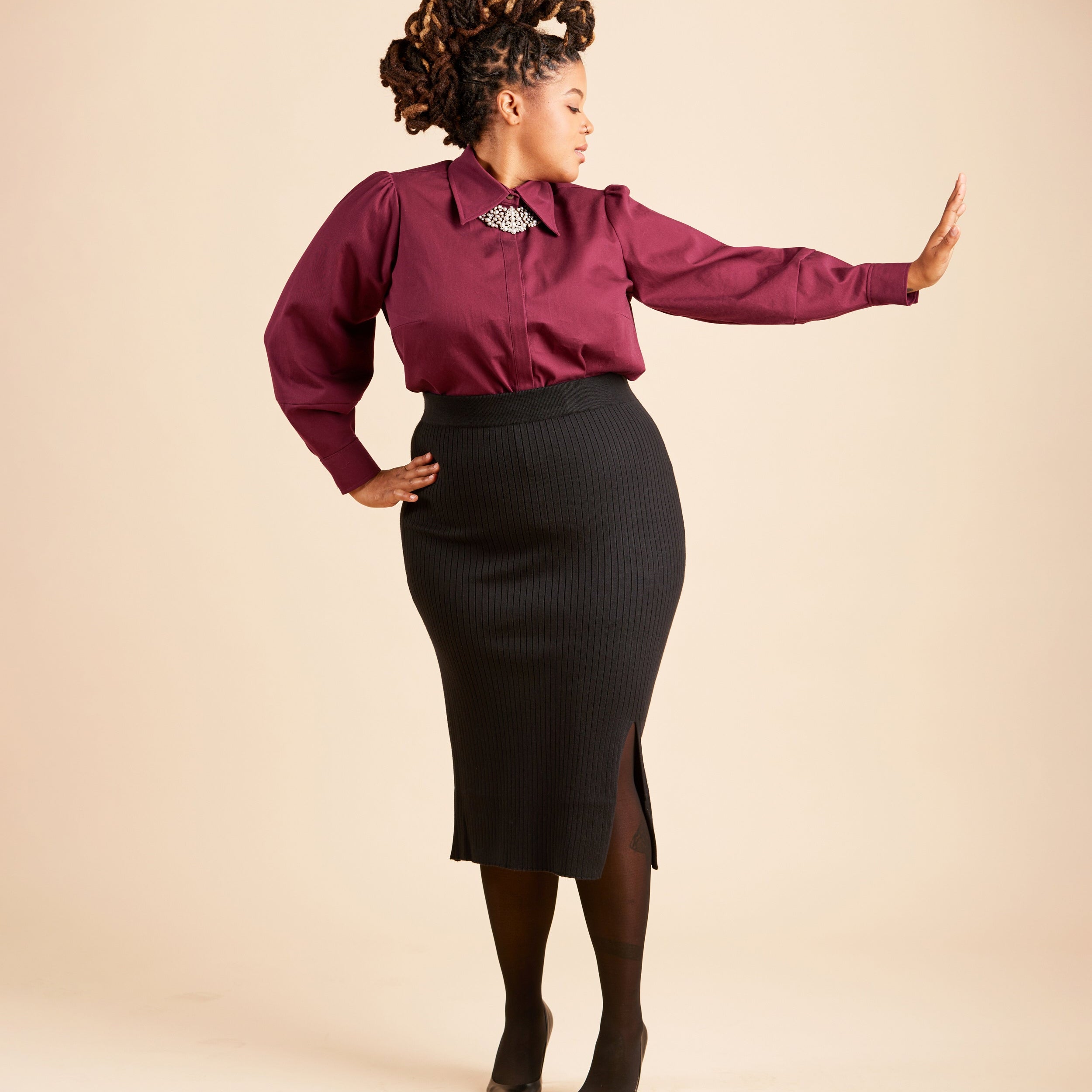 Woman wearing a burgundy blouse and black skirt against a beige background. This top is the Vernon Shirt sewing pattern from Cashmerette.