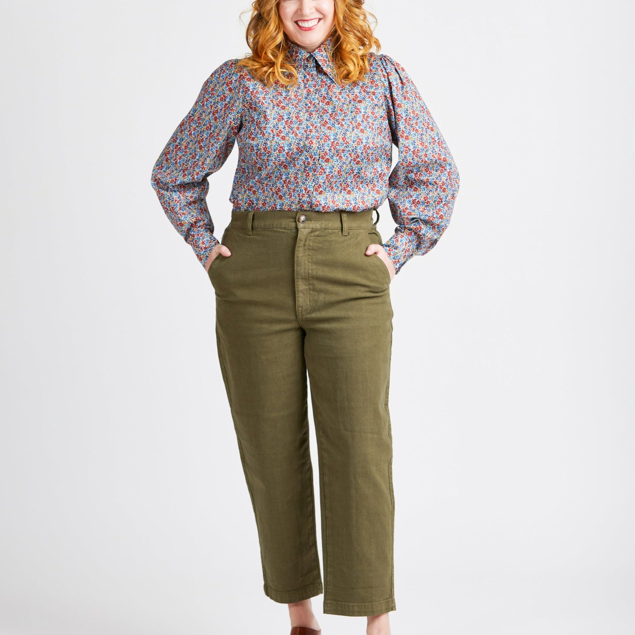Woman wearing a floral blouse and green pants on a white background. This top is the Vernon Shirt sewing pattern from Cashmerette.
