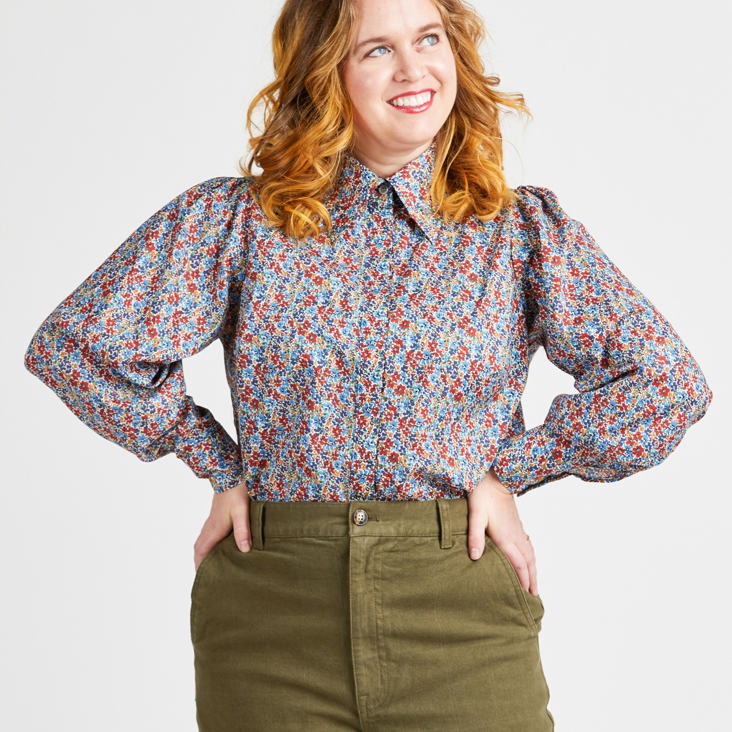 Woman wearing a floral blouse and green pants against a plain background. This top is the Vernon Shirt sewing pattern from Cashmerette.