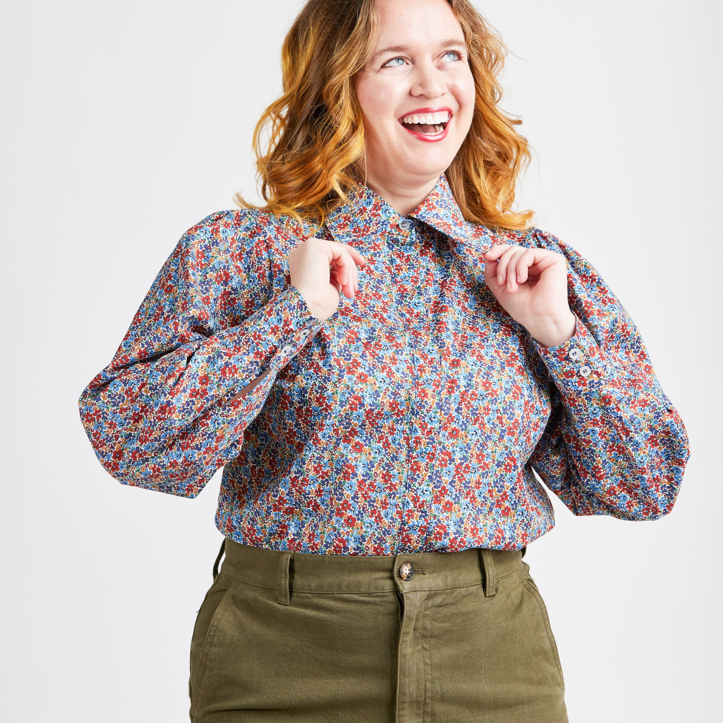 Woman wearing a floral blouse and green pants on a white background. This top is the Vernon Shirt sewing pattern from Cashmerette.