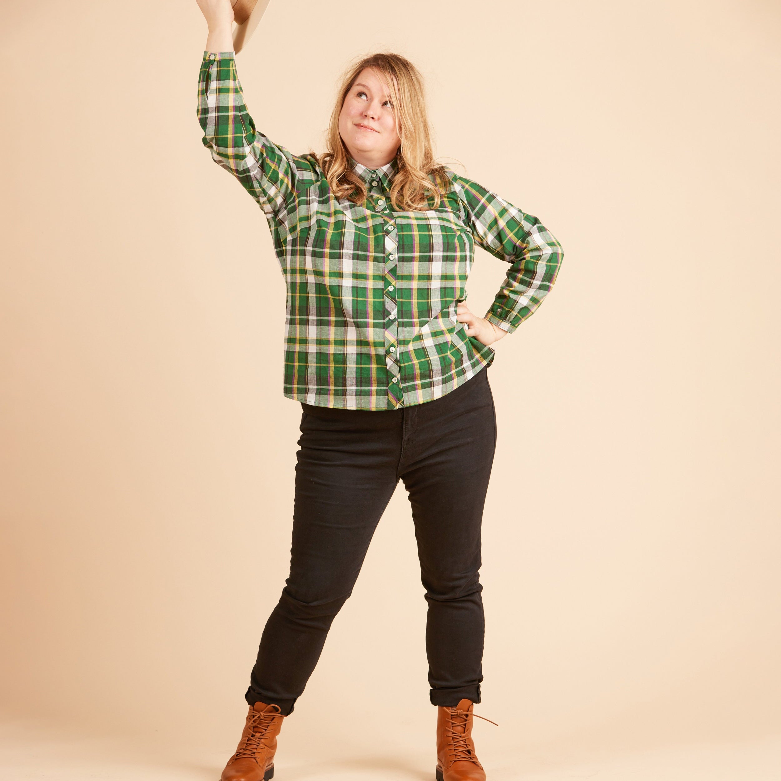 Person wearing a green plaid shirt, black pants, and brown boots against a beige background. This top is the Vernon Shirt sewing pattern from Cashmerette.