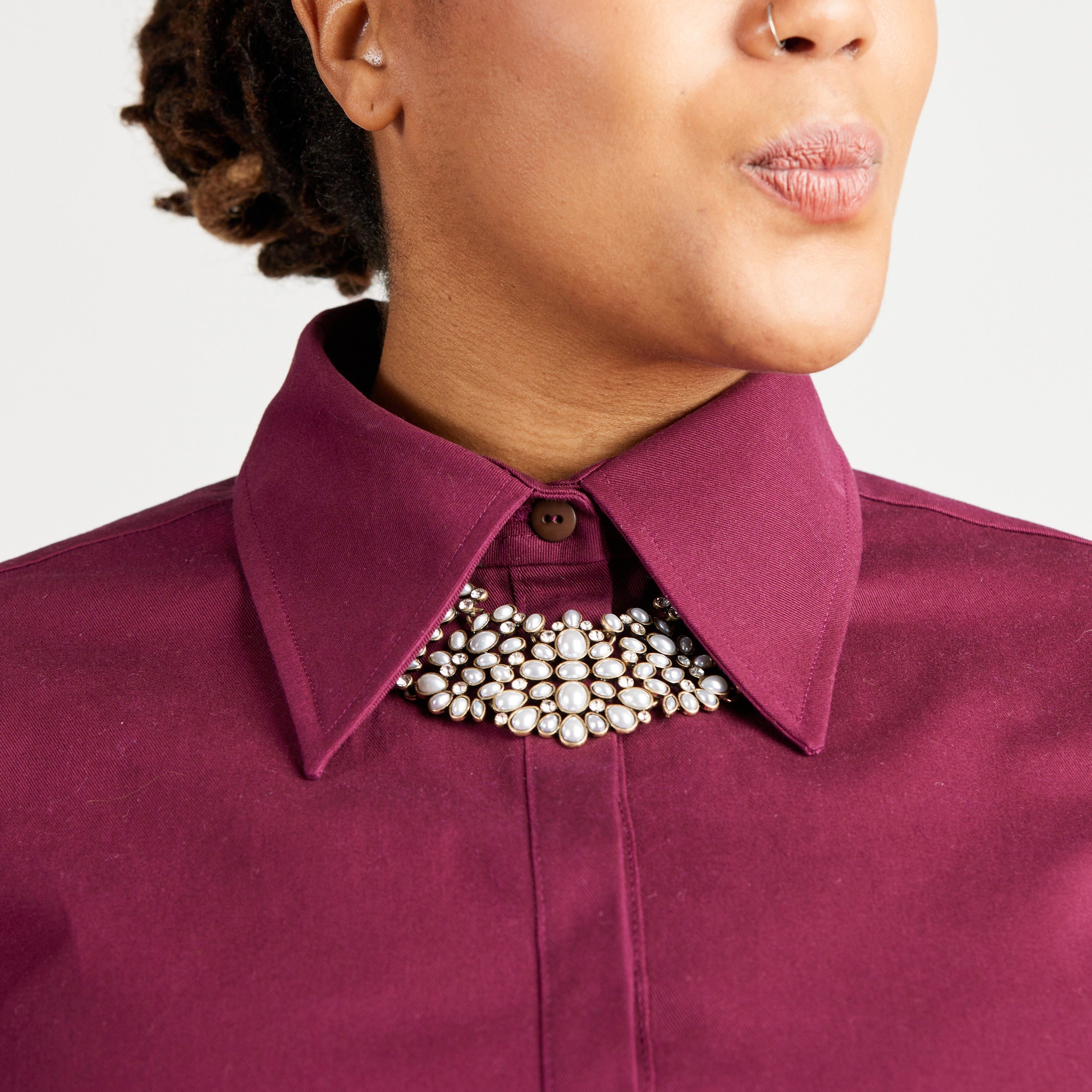 Close-up of a person wearing a purple shirt with a pearl necklace against a white background. This top is the Vernon Shirt sewing pattern from Cashmerette.