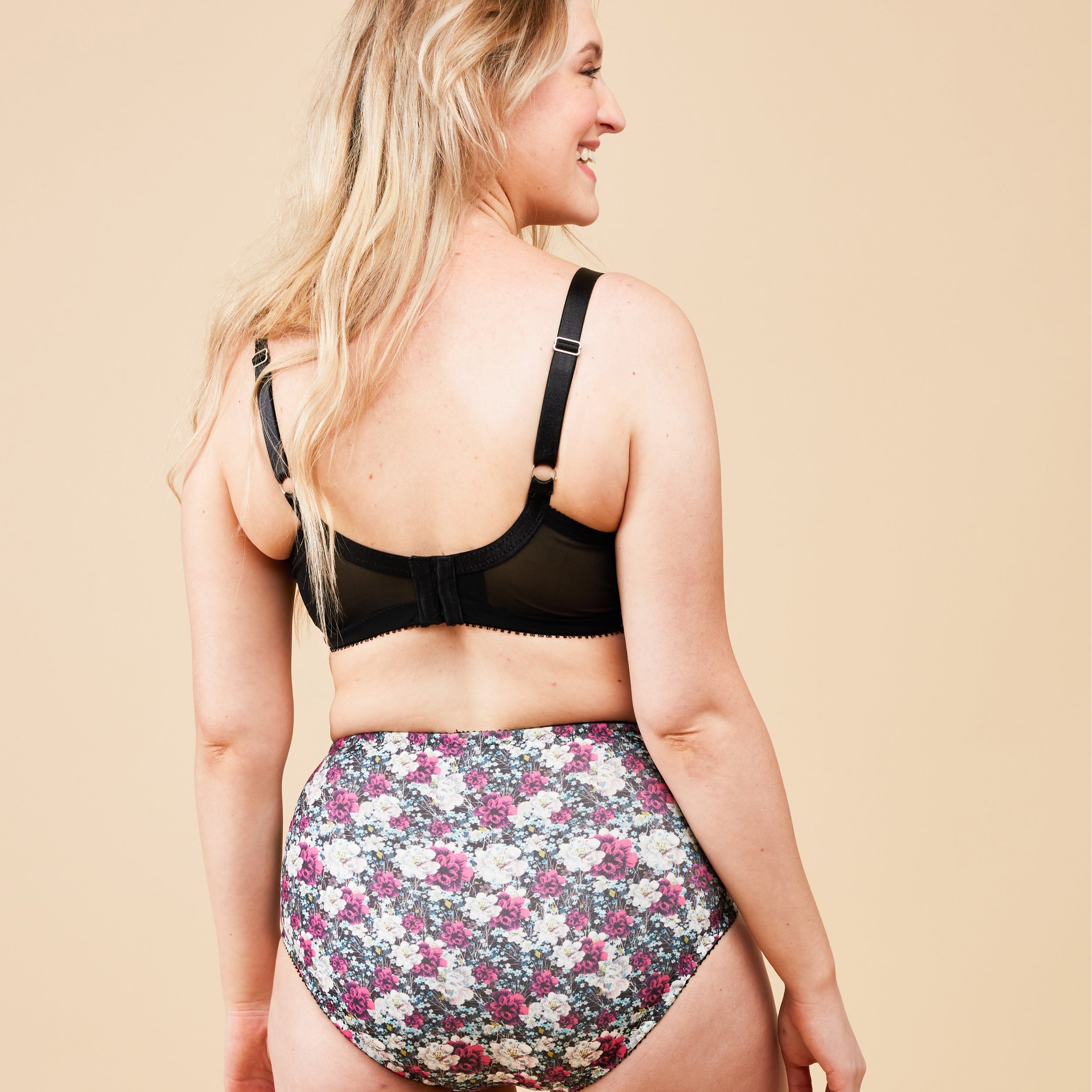 Woman wearing a black bra and floral high-waisted underwear on a beige background. This bra is the Willowdale Bra sewing pattern from Cashmerette.
