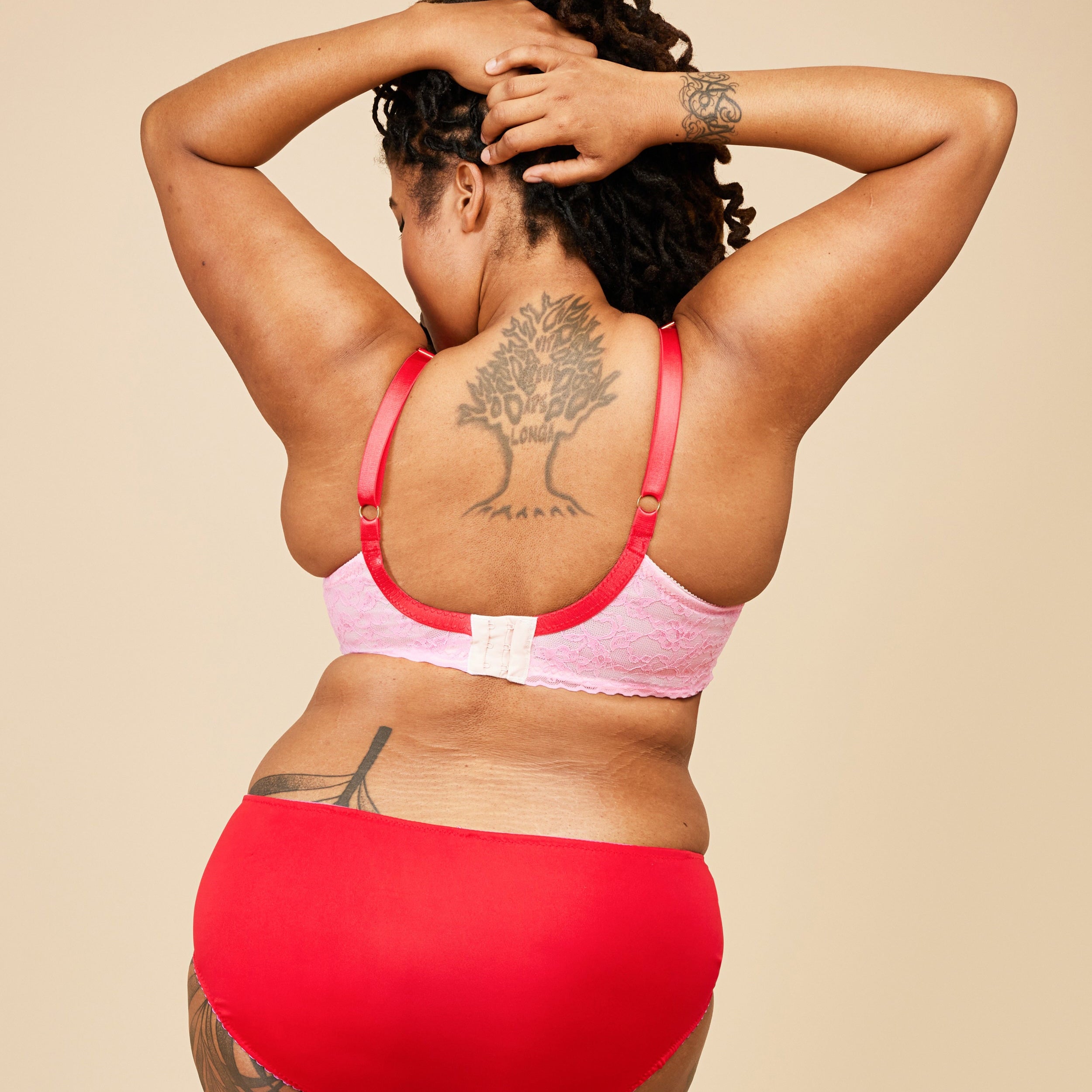 Person wearing a pink bikini top and red bottoms against a beige background. This bra is the Willowdale Bra sewing pattern from Cashmerette.