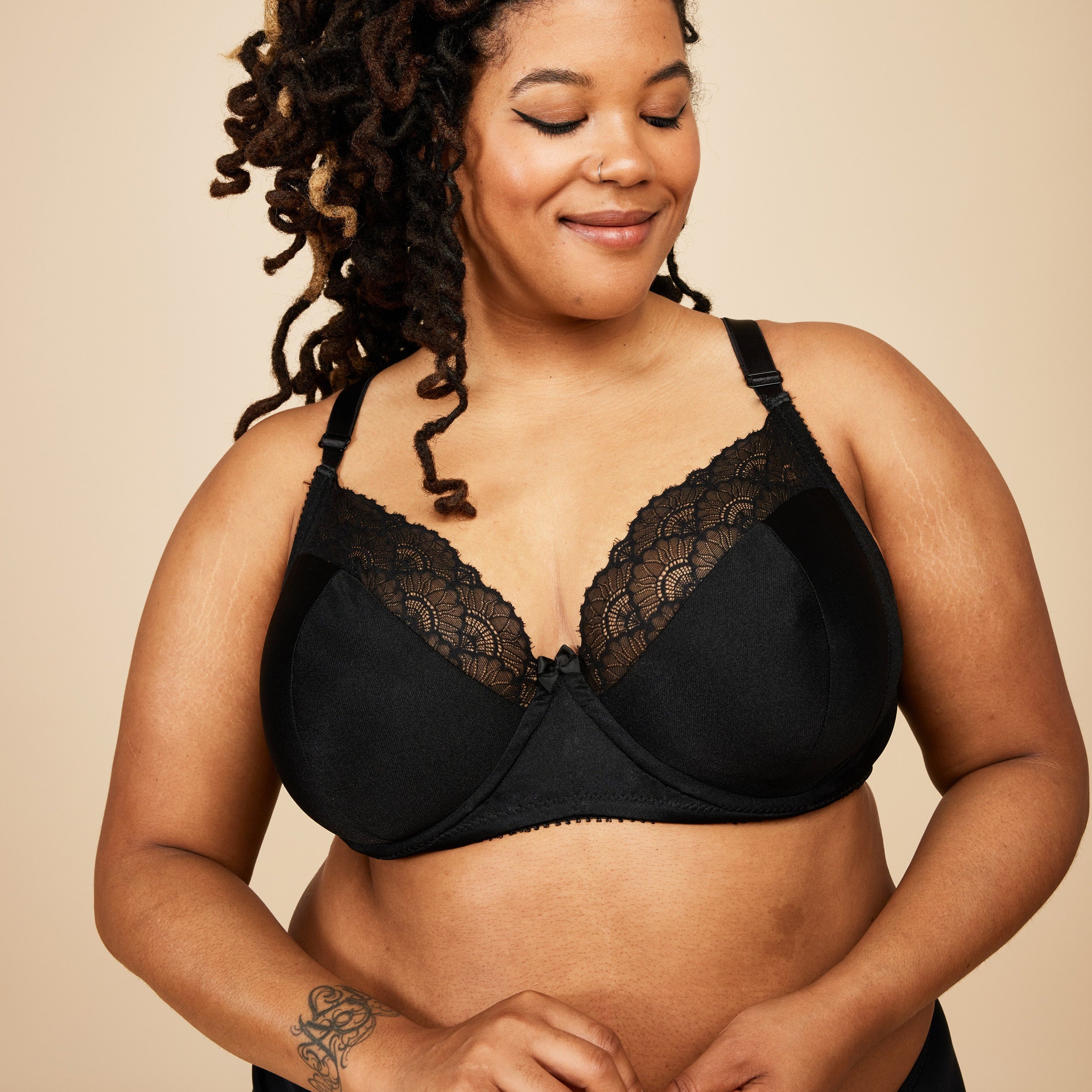 Woman wearing a black lace bra against a beige background. This bra is the Willowdale Bra sewing pattern from Cashmerette.