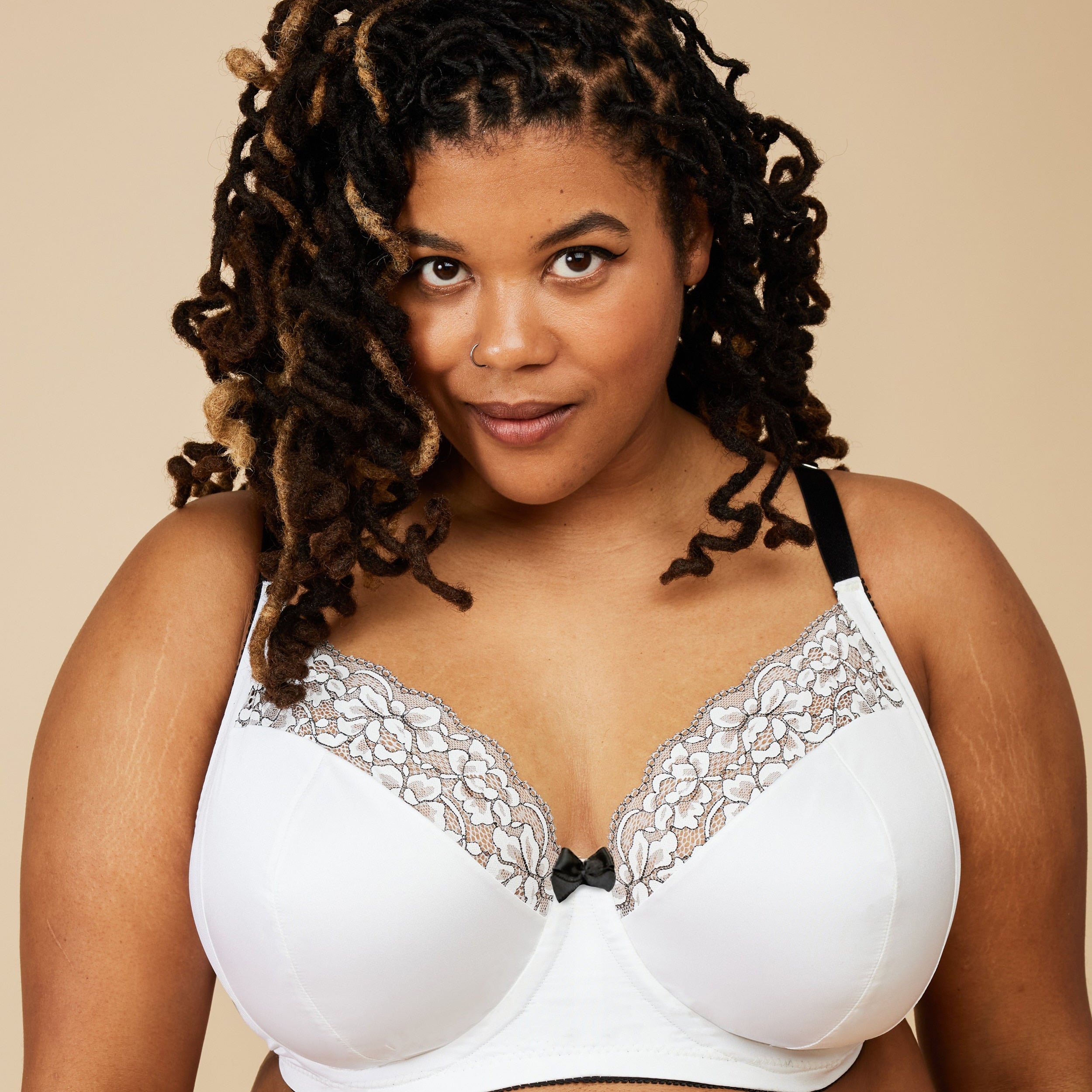 Woman wearing a white bra with lace details against a beige background. This bra is the Willowdale Bra sewing pattern from Cashmerette.