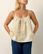 Woman wearing a beige tank top and blue pants against a plain background