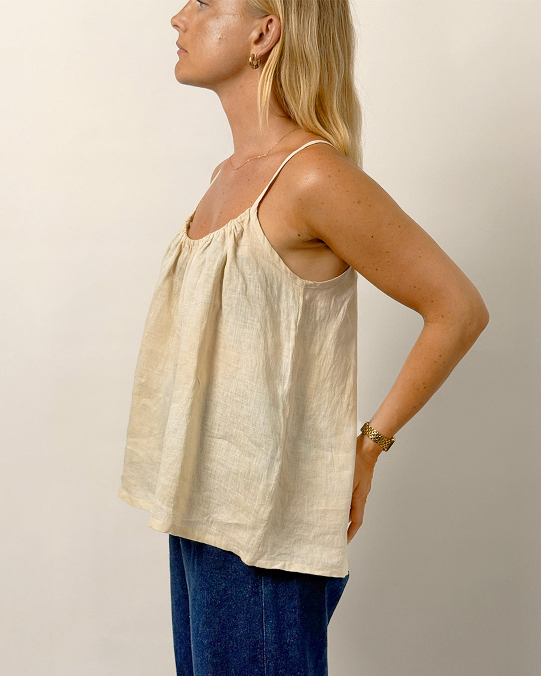 Woman wearing a beige sleeveless top and blue pants against a plain background