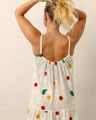 Woman wearing a white dress with colorful floral patterns on a plain background