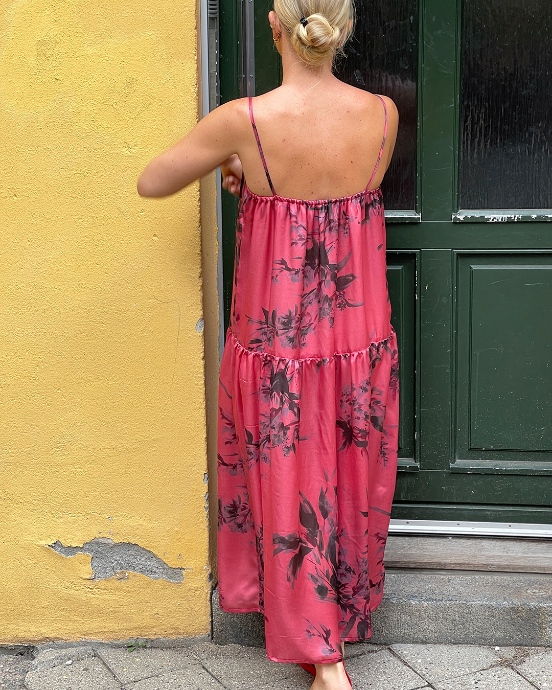 Woman wearing a pink floral dress standing in front of a yellow wall and green door.