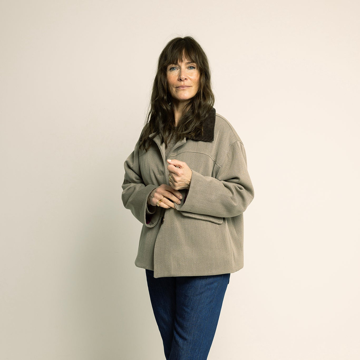 Woman wearing a beige jacket and blue pants on a plain background