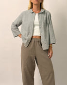 Woman wearing a checkered jacket, white top, and brown pants on a plain background
