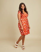 Woman wearing a red dress with white patterns on a beige background. This dress is the Appleton Wrap Dress sewing pattern from Cashmerette.