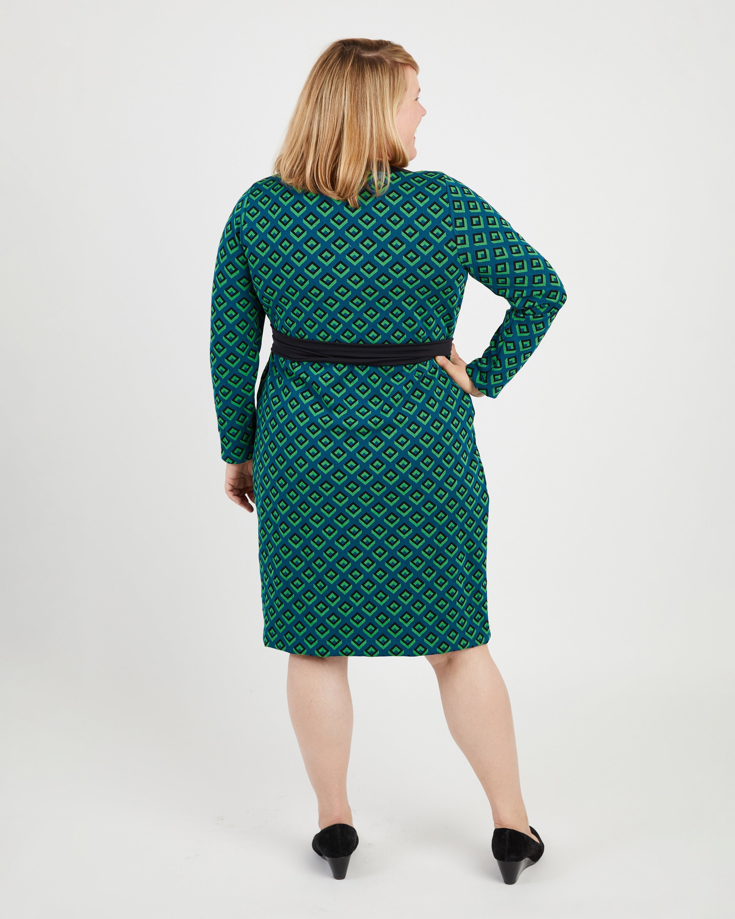Woman wearing a green patterned dress on a white background. This dress is the Appleton Wrap Dress sewing pattern from Cashmerette.