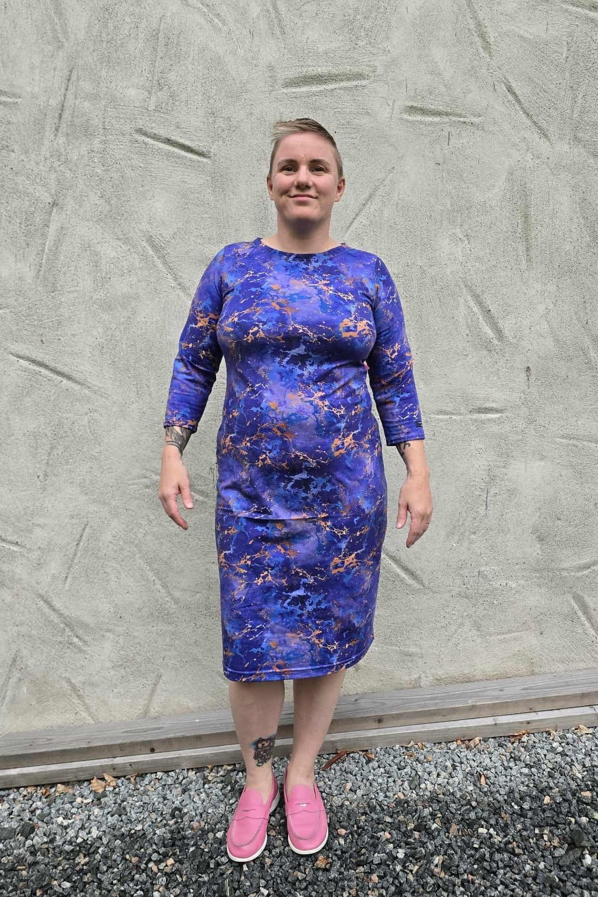 Person wearing a blue floral dress standing against a textured gray wall.