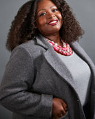 Woman wearing a gray coat and pink necklace against a gray background. This blazer is the Auburn Blazer sewing pattern from Cashmerette.