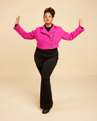 Person wearing a bright pink jacket and black pants on a beige background. This biker jacket is the Canton Moto Jacket sewing pattern from Cashmerette.