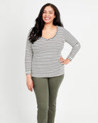 A woman standing, wearing a striped long-sleeved t-shirt and green pants. This t-shirt is the Concord T-Shirt sewing pattern from Cashmerette.