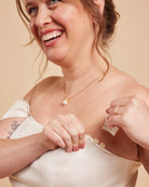 Woman wearing a gold necklace with a pearl pendant against a beige background. This dress is the Ellington Strapless Dress sewing pattern from Cashmerette.