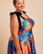 Woman wearing a colorful floral dress with a bow detail on a beige background. This dress is the Ellington Strapless Dress sewing pattern from Cashmerette.