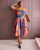 Woman wearing a strapless dress with blue floral pattern against a pink paneled wall. This dress is the Ellington Strapless Dress sewing pattern from Cashmerette.