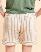 Beige shorts with black stripes worn by a person on a beige background. These shorts are the Everett Pants & Shorts sewing pattern from Cashmerette.