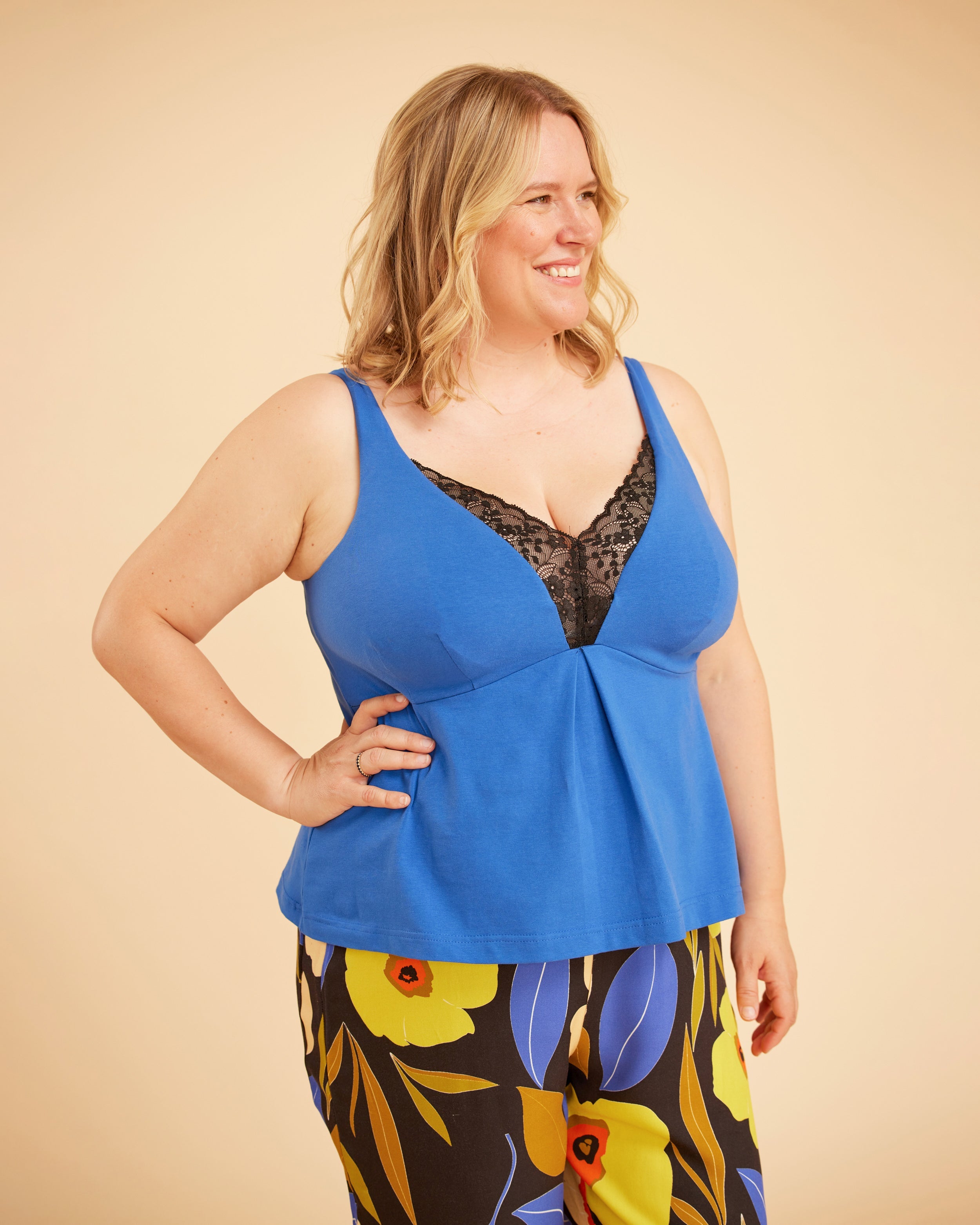 Woman wearing a blue top with floral pants on a beige background. This is the Fiske Sleepwear Set sewing pattern from Cashmerette.