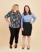 Two women standing side by side against a beige background, wearing colorful shirts and black pants.. This button-up shirt is the Harrison Shirt sewing pattern from Cashmerette.