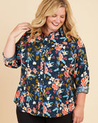 Woman wearing a floral blouse on a beige background. This button-up shirt is the Harrison Shirt sewing pattern from Cashmerette.