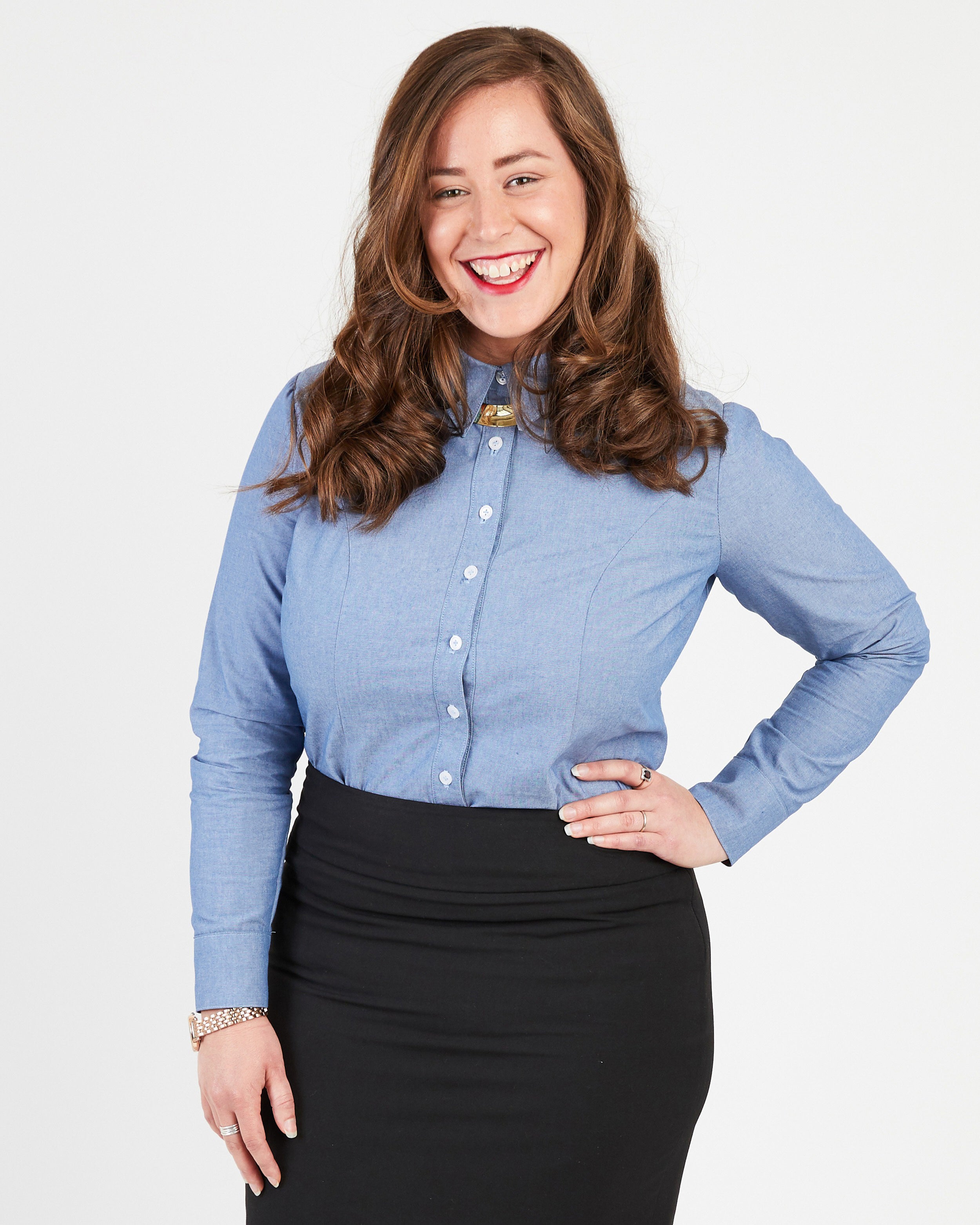 Woman wearing a blue button-up shirt and black skirt on a white background. This button-up shirt is the Harrison Shirt sewing pattern from Cashmerette.