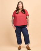 Person wearing a red shirt and blue jeans on a beige background. This is the Montrose Top sewing pattern from Cashmerette.