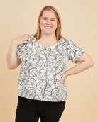 Woman wearing a black and white patterned top and black pants on a beige background. This is the Montrose Top sewing pattern from Cashmerette.