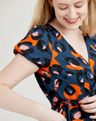 Woman wearing a blue dress with orange and black abstract pattern. This dress is the Roseclair Wrap Dress sewing pattern from Cashmerette.