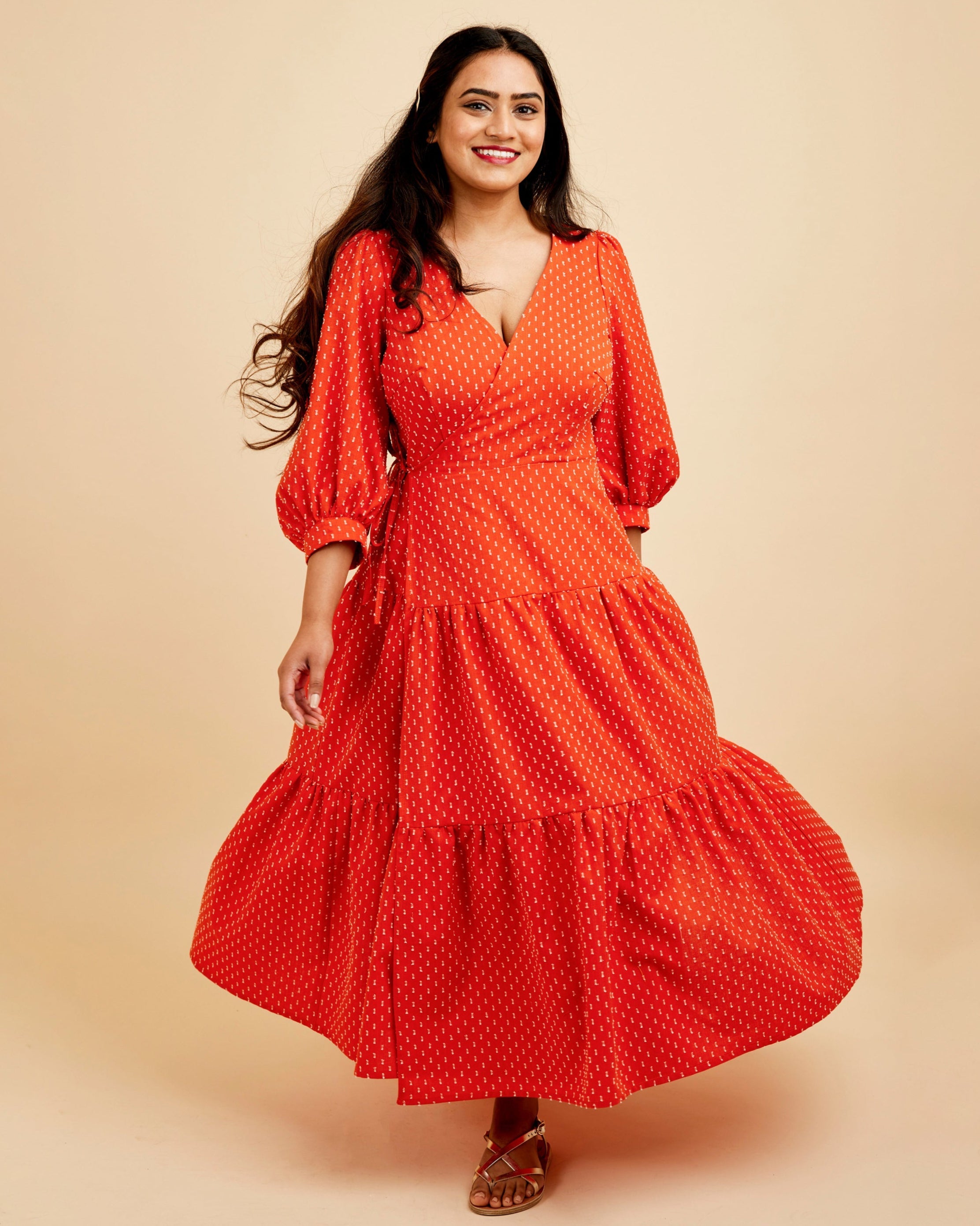 Woman wearing a red polka dot dress on a beige background. This dress is the Roseclair Wrap Dress sewing pattern from Cashmerette.