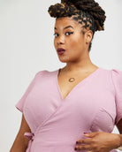 Woman wearing a pink dress against a white background. This dress is the Roseclair Wrap Dress sewing pattern from Cashmerette.