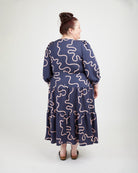 Woman wearing a navy dress with pink wavy patterns on a white background. This dress is the Roseclair Wrap Dress sewing pattern from Cashmerette.