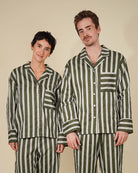 A man and a woman modeling matching green and white vertically striped pajama sets against a solid beige background.